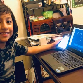A smiling child at a desk with a laptop open in front of them.